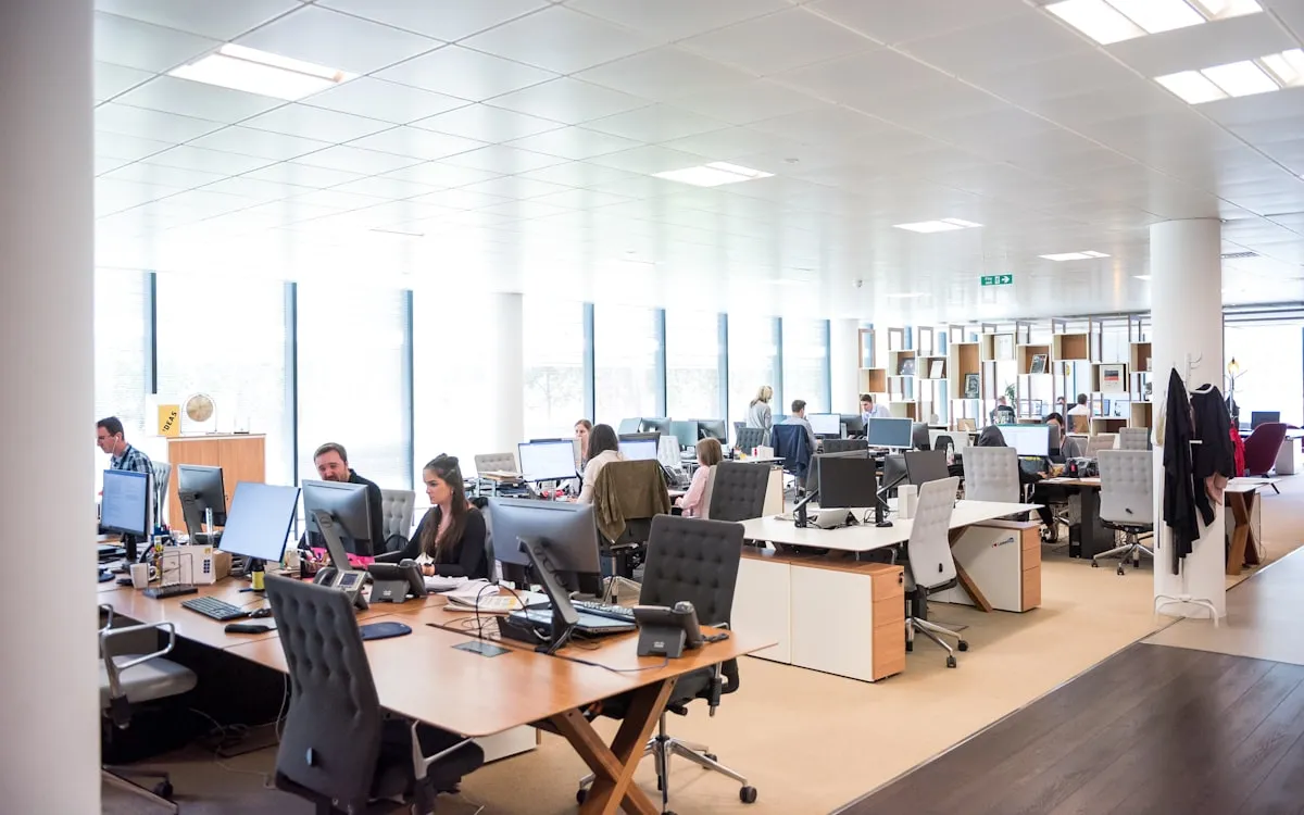 A bright open-plan office floor of desks and administrative workstations.